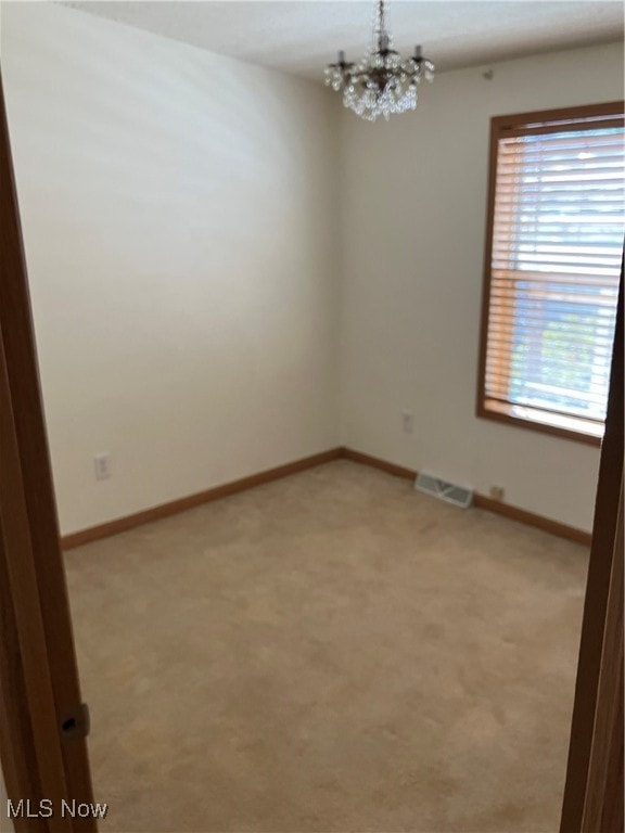 carpeted empty room featuring a chandelier