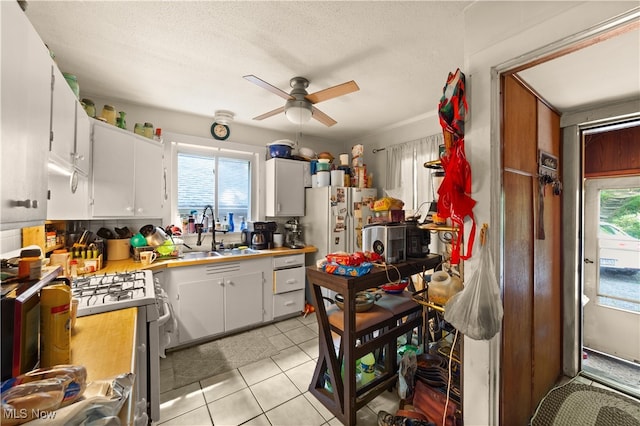 kitchen featuring gas stove, ceiling fan, sink, light tile patterned floors, and white cabinets