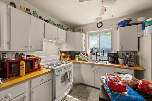 kitchen featuring decorative backsplash, white gas range, ceiling fan, sink, and white cabinetry