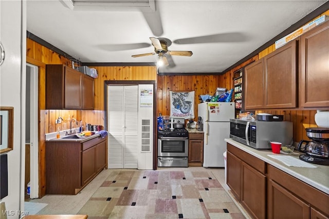 kitchen with ceiling fan, sink, stainless steel appliances, and wooden walls