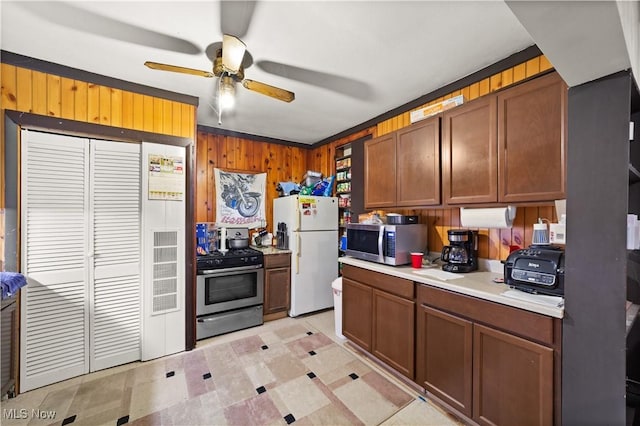 kitchen with wooden walls, ceiling fan, ornamental molding, and appliances with stainless steel finishes