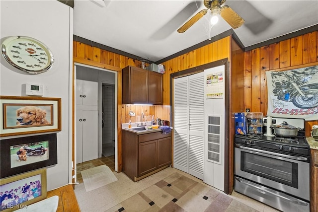 kitchen featuring stainless steel gas stove, backsplash, crown molding, and wood walls