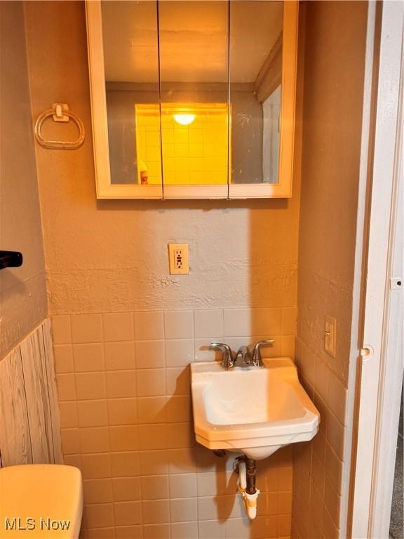 bathroom with toilet, tile walls, and sink