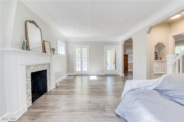 bedroom featuring a textured ceiling, light wood-type flooring, french doors, and a fireplace