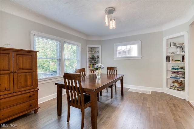 dining area with a textured ceiling, hardwood / wood-style floors, and built in shelves