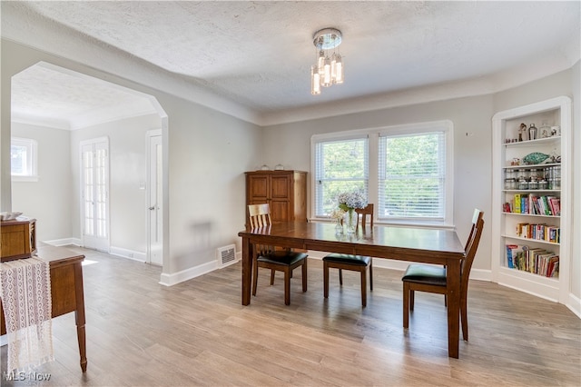 dining area with a textured ceiling, a notable chandelier, light hardwood / wood-style floors, built in shelves, and ornamental molding