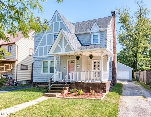 tudor house featuring covered porch, an outdoor structure, a garage, and a front lawn