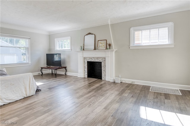 unfurnished bedroom with ornamental molding, light hardwood / wood-style floors, a textured ceiling, and a stone fireplace