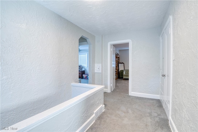 hallway featuring a textured ceiling and light colored carpet