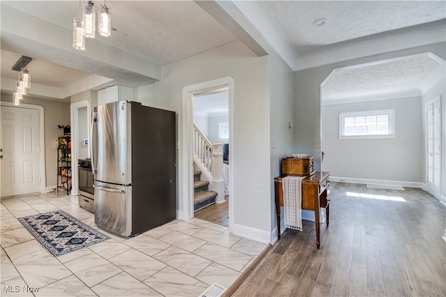 kitchen with decorative light fixtures, light hardwood / wood-style floors, a notable chandelier, stainless steel refrigerator, and a textured ceiling