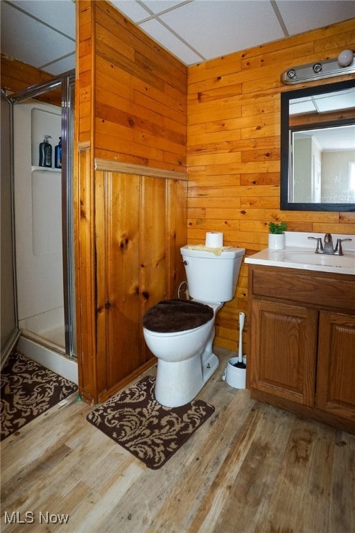 bathroom with hardwood / wood-style flooring, wooden walls, walk in shower, toilet, and vanity