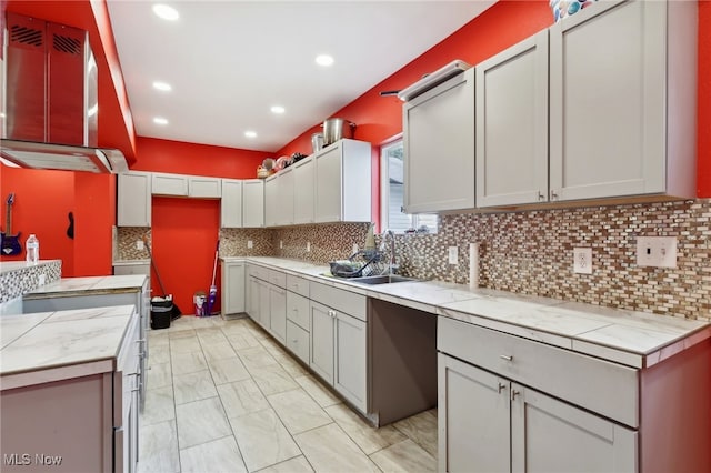 kitchen with tasteful backsplash, sink, gray cabinetry, and wall chimney range hood