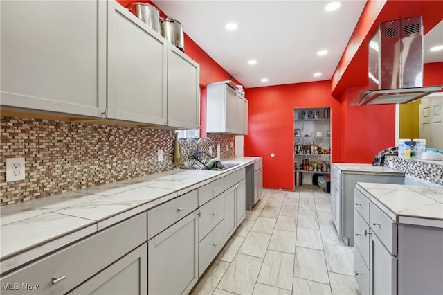 kitchen featuring backsplash, gray cabinetry, and wall chimney range hood