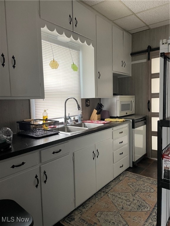 kitchen featuring white cabinets, dark tile patterned floors, a barn door, sink, and a drop ceiling