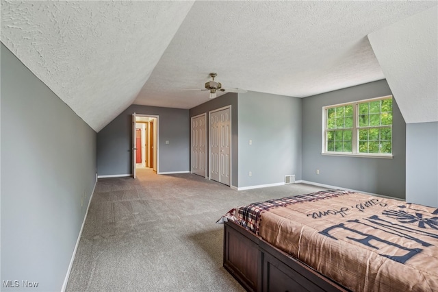 carpeted bedroom with vaulted ceiling, multiple closets, ceiling fan, and a textured ceiling