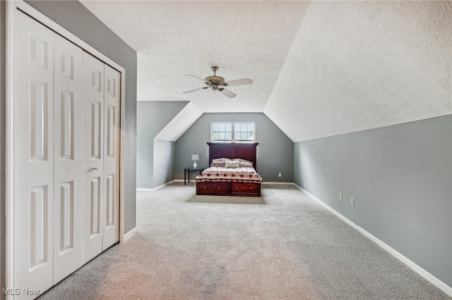 unfurnished bedroom featuring ceiling fan, lofted ceiling, a textured ceiling, light carpet, and a closet