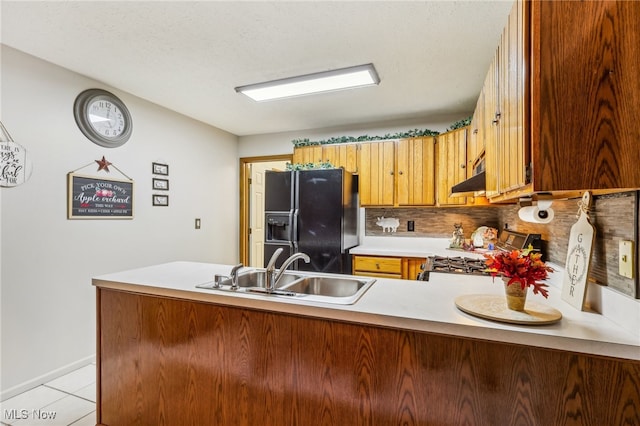 kitchen featuring kitchen peninsula, backsplash, black refrigerator with ice dispenser, sink, and stainless steel range oven