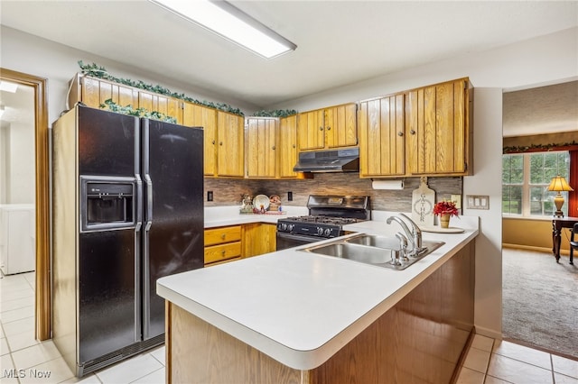 kitchen with kitchen peninsula, stainless steel gas range oven, black fridge with ice dispenser, sink, and light tile patterned floors