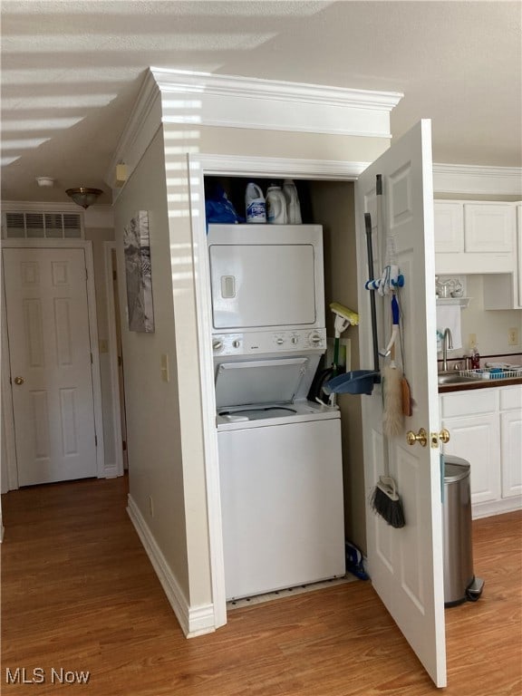 clothes washing area with light wood-type flooring, crown molding, and stacked washer / drying machine