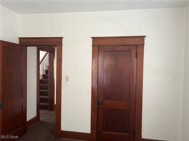 hall featuring a textured ceiling and dark colored carpet