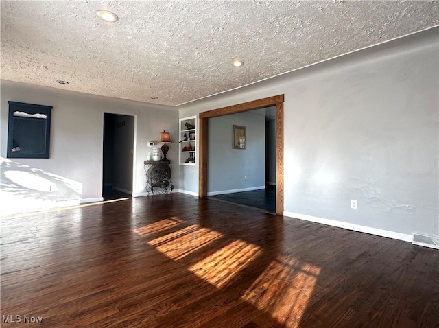 empty room with built in shelves, dark wood-type flooring, and a textured ceiling