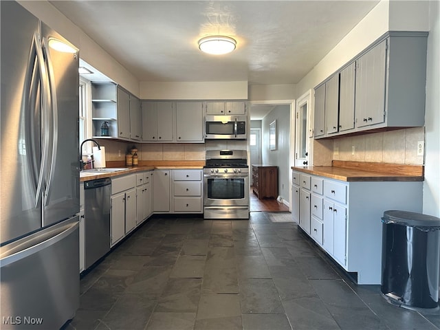 kitchen featuring sink, butcher block countertops, gray cabinetry, appliances with stainless steel finishes, and backsplash