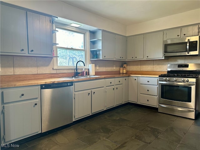 kitchen featuring sink, wooden counters, appliances with stainless steel finishes, white cabinets, and backsplash