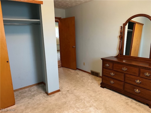 unfurnished bedroom featuring a textured ceiling, a closet, and light carpet