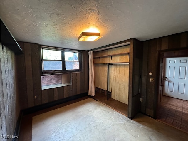 unfurnished bedroom featuring a textured ceiling, a closet, wooden walls, and concrete flooring