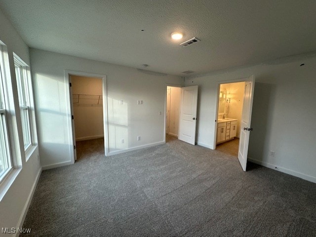 unfurnished bedroom featuring a walk in closet, dark carpet, a textured ceiling, connected bathroom, and a closet