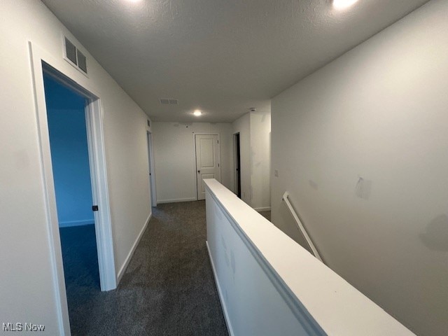 corridor with a textured ceiling and dark colored carpet