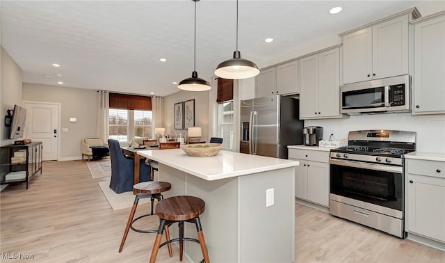 kitchen with gray cabinets, light wood-type flooring, decorative light fixtures, a kitchen island, and stainless steel appliances