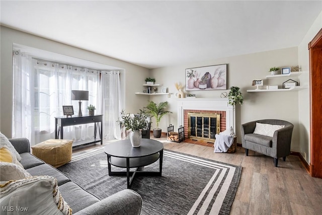 living area featuring a brick fireplace, baseboards, and wood finished floors