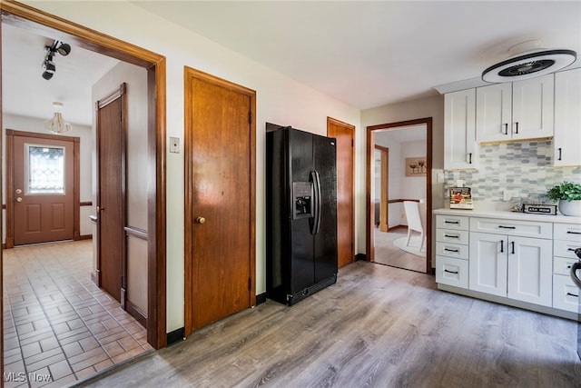 kitchen with white cabinetry, backsplash, black refrigerator with ice dispenser, and light hardwood / wood-style flooring