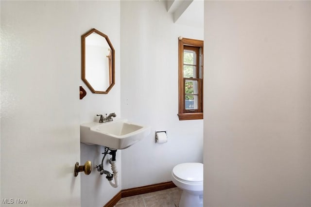 half bath with toilet, tile patterned flooring, baseboards, and a sink