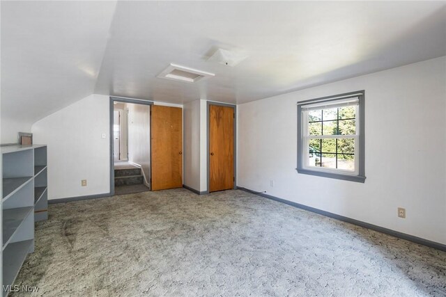 unfurnished bedroom featuring attic access, lofted ceiling, carpet, and baseboards