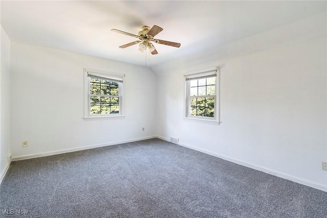 empty room featuring baseboards, dark carpet, and a wealth of natural light