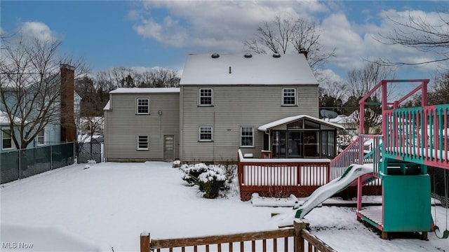 snow covered rear of property with a playground, a deck, and a sunroom