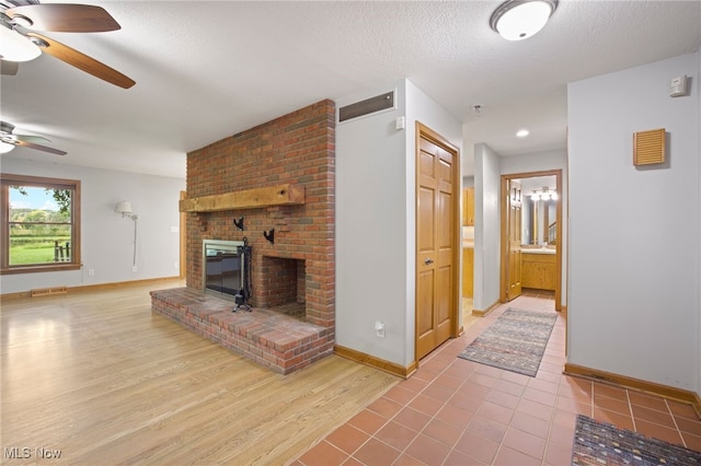 living room with a fireplace, a textured ceiling, ceiling fan, and light hardwood / wood-style floors