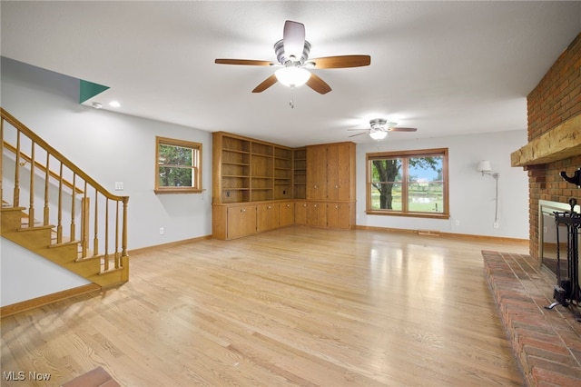 unfurnished living room featuring a fireplace, light wood-type flooring, a wealth of natural light, and ceiling fan