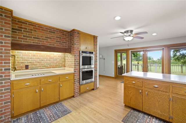 kitchen with brick wall, light hardwood / wood-style floors, stainless steel double oven, ceiling fan, and black electric cooktop