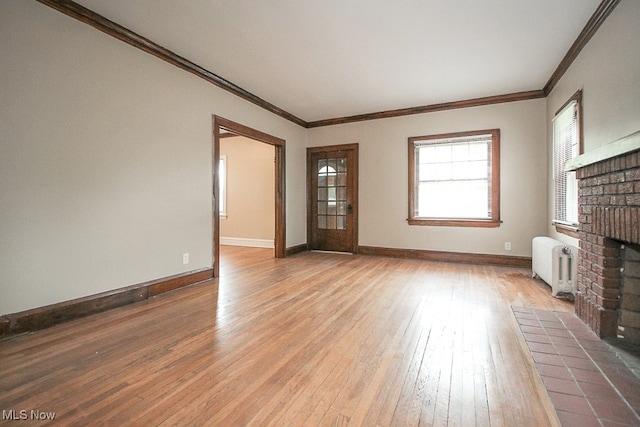 unfurnished living room with crown molding, radiator, a brick fireplace, and hardwood / wood-style floors