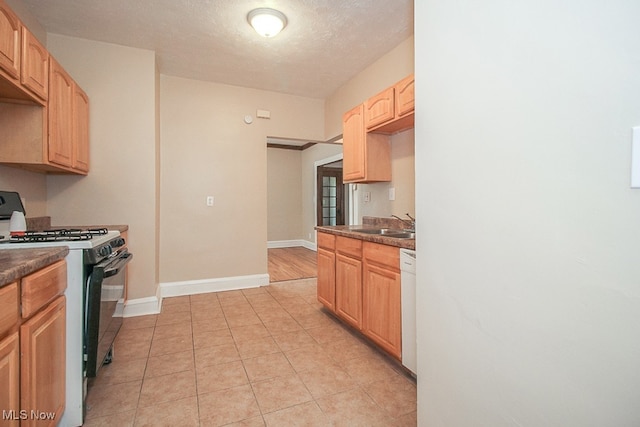 kitchen featuring light brown cabinetry, white dishwasher, stainless steel range with gas cooktop, and a textured ceiling