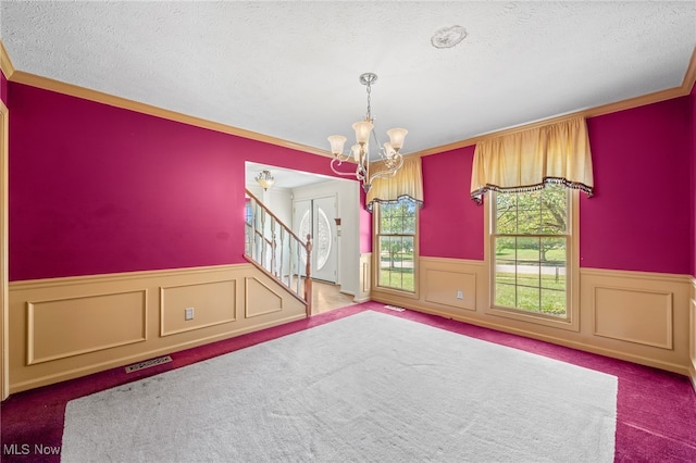 carpeted empty room with crown molding, a textured ceiling, and a chandelier