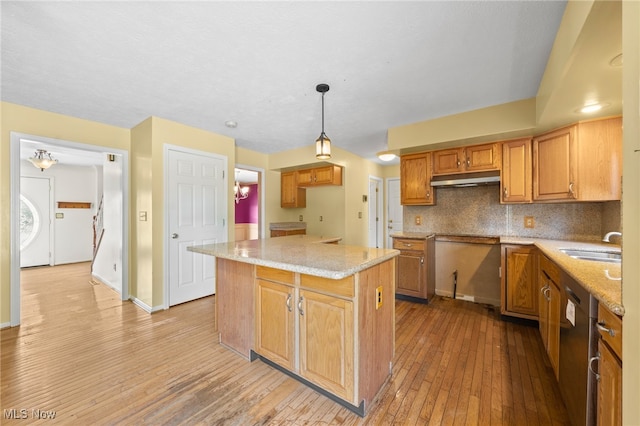 kitchen featuring decorative light fixtures, light wood-type flooring, a kitchen island, tasteful backsplash, and stainless steel dishwasher