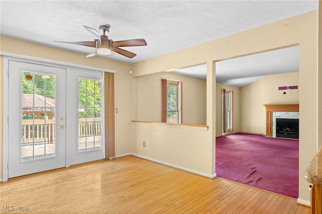 spare room featuring french doors, light colored carpet, a premium fireplace, ceiling fan, and a textured ceiling