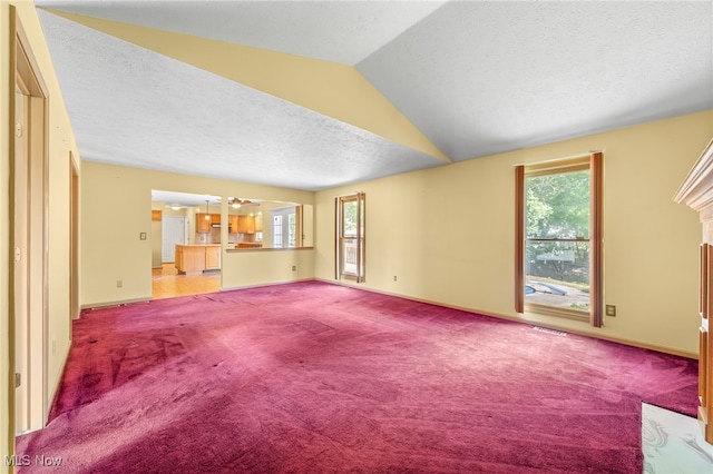 unfurnished living room with plenty of natural light, a textured ceiling, light carpet, and vaulted ceiling