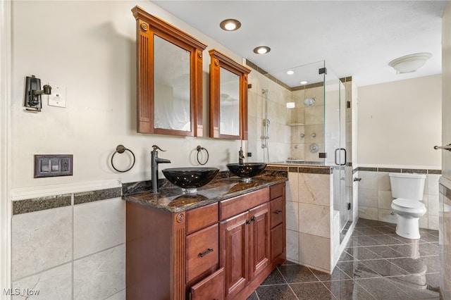 bathroom with a shower with door, tile walls, toilet, and vanity