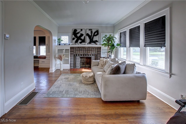 living room featuring a fireplace, dark wood-type flooring, crown molding, and plenty of natural light