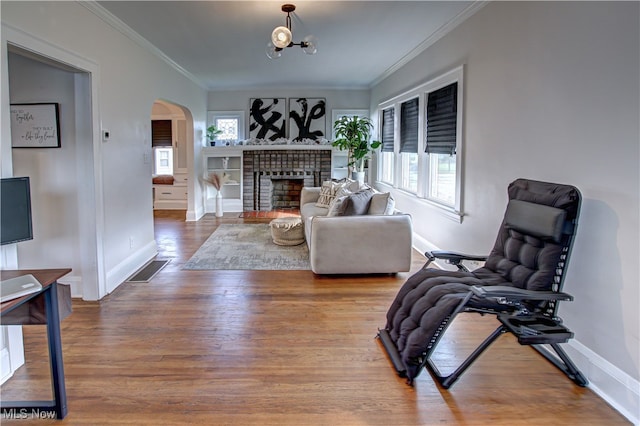 living room with ornamental molding, hardwood / wood-style flooring, a wealth of natural light, and a brick fireplace